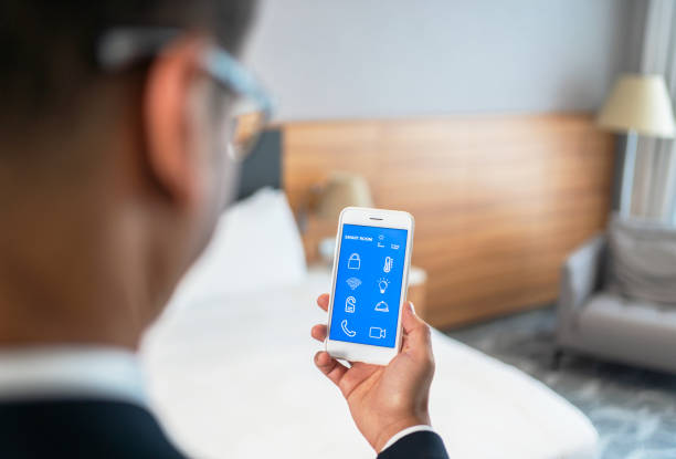 istock Businessman Using Smart Room Application On Smartphone screen İn Hotel Room 1327763149