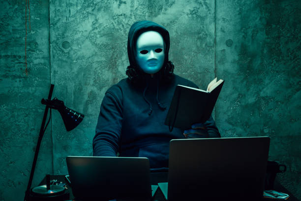 Anonymous hacker wearing face mask working on computer in dark room Anonymous hacker wearing face mask working on computer in dark room, close up anonymous activist network stock pictures, royalty-free photos & images