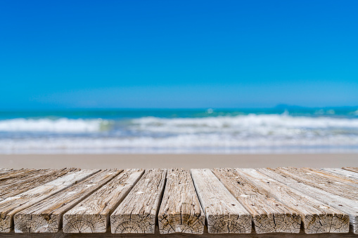 Empty rustic wooden table with defocused lonely sand beach at background. Ideal for product display on top of the table. Predominant color are blue and brown. XXXL 42Mp outdoors photo taken with SONY A7rII and Zeiss Batis 40mm F2.0 CF