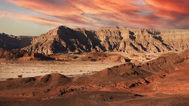 Evening landscape of the Arava desert in red colors. Red mountains, sand and orange clouds in the evening desert.