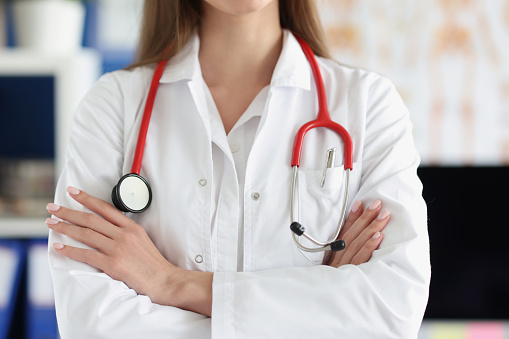 Woman doctor with red stethoscope standing in uniform with folded hands closeup. Professional medical advice concept