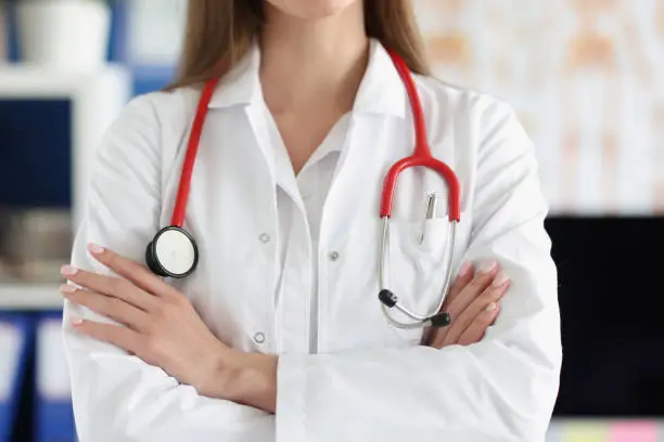 Photo of Woman doctor with red stethoscope standing in uniform with folded hands closeup