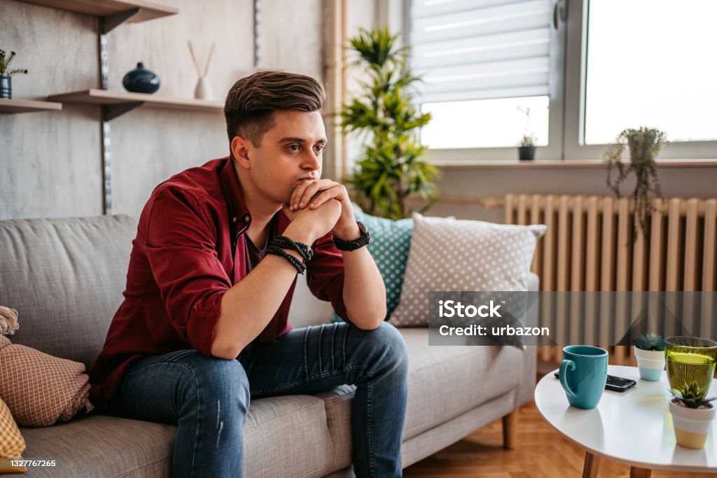 Man sitting alone at home looking sad and distraught Man looking depressed while sitting alone with his head in his hand on his living room sofa at home. Men Stock Photo
