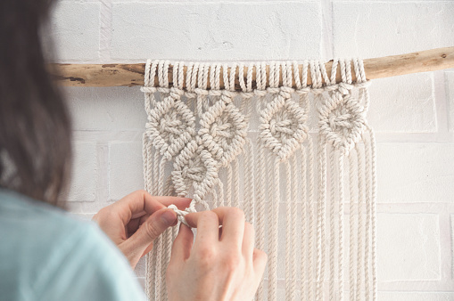 Boho wall mural made of natural color cotton threads using macrame technique for home and wedding decor in the production process