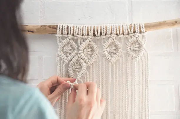 Photo of Boho wall mural made of natural color cotton threads using macrame technique for home and wedding decor in the production process