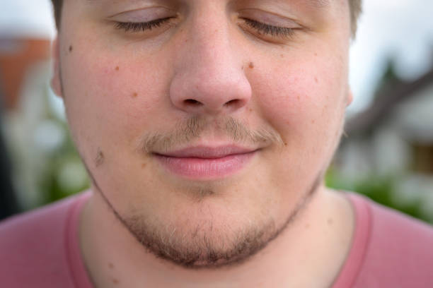 Man with wispy goatee beard and moustache posing with closed eyes and a quiet smile in a close up cropped view of his face