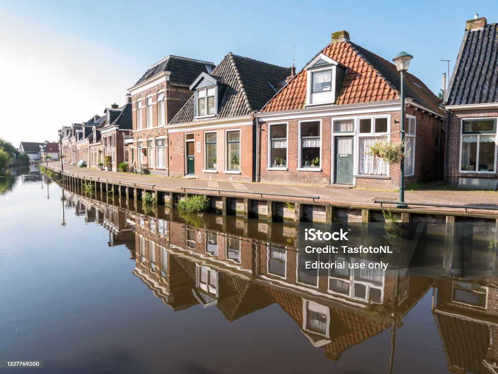 Row of houses reflecting in canal in Warga, Leeuwarden, Friesland, Netherlands Row of houses reflecting in Wargaastervaart canal in village of Wergea, Leeuwarden, Friesland, Netherlands Leeuwarden Stock Photo