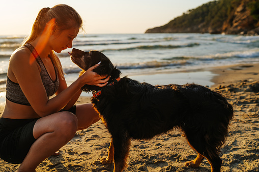 Beautiful young woman kissing with her dog on the beach at sunrise