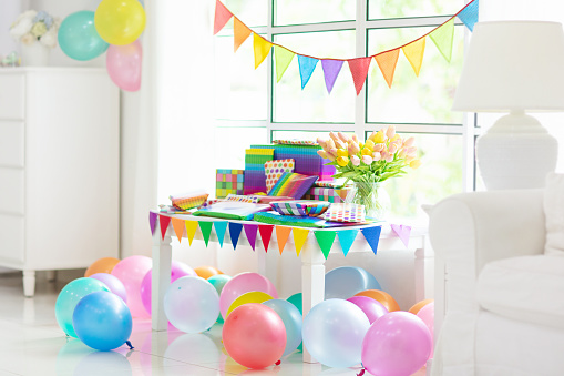 Presents at birthday party. Colorful wrapped gifts. Rainbow theme event for kids. Children celebration at home. Table with present at a big window with banner and balloons.