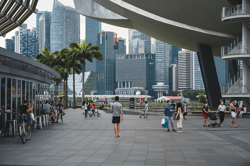 People walking on the Marina Bay promenade in Singapore. The promenade is surrounded by big skyscrapers and shopping malls.