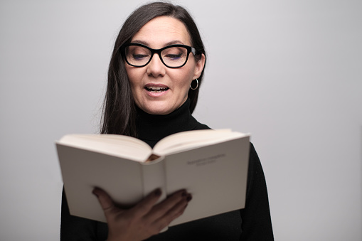 A woman holding a book and reading out loud.