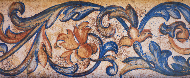 detail of a border painted on a tile with red, orange and blue flowers