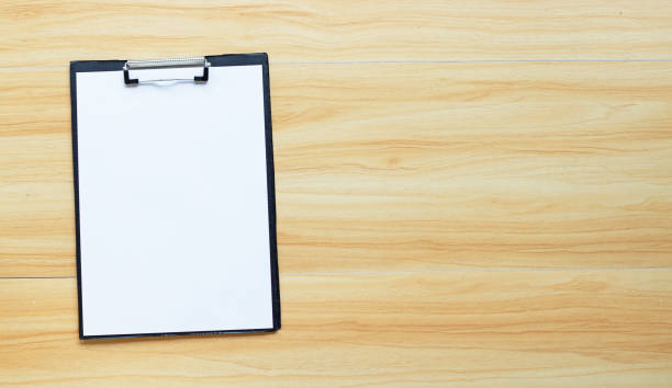 istock Blank a4 paper in black clipboard on wooden background. 1327781765