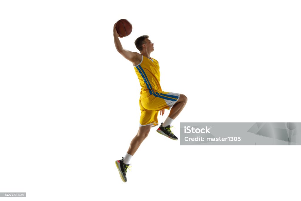 Side view. One young man, basketball player with a ball training isolated on white studio background. Advertising concept. Fit Caucasian athlete jumping with ball. Side view. Young man, basketball player with a ball training isolated on white studio background. Advertising concept. Sportive Caucasian athlete playing basketball. Motion, activity, movement concepts. Basketball Player Stock Photo