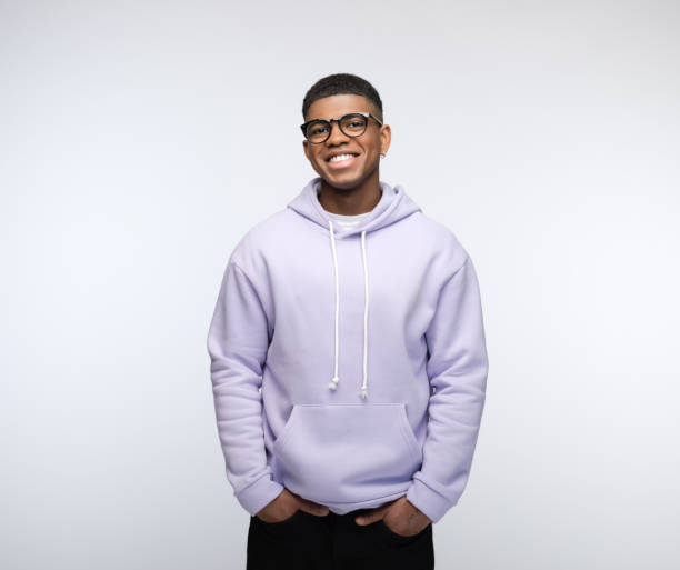 Cheerful young man wearing lilac hoodie Happy african young man wearing lilac hoodie, standing with hands in pockets and laughing at camera. Studio portrait on white background. MAN WEAR Hoodie stock pictures, royalty-free photos & images