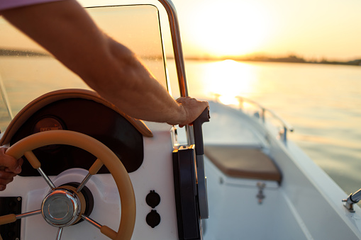 Close-up shot of a man's hand on a speedboat's steering wheel at sunset on the Danube river.