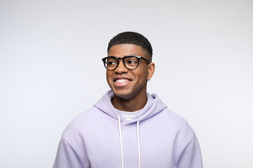 Confident african young man wearing lilac hoodie, looking away and laughing. Studio portrait on white background.