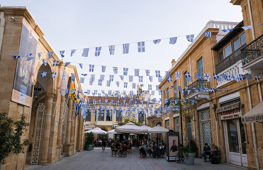 Nicosia, Cyprus, April 17 2021: People relaxing at coffee shops and greek flags waving for celebration of Greece independence. Leadra street, Nicosia Cyprus