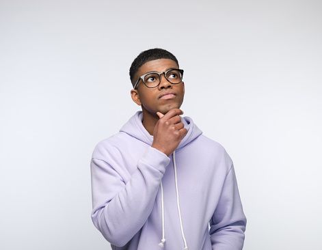 Pensive african young man wearing lilac hoodie, looking away with hand on chin. Studio portrait on white background.