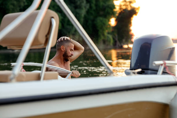 Young man enjoying the vacation on the seaside, driving a speedboat in the Adriatic seas of the Mediterranean, lit by the hot bright sunshine. Happiness, summertime concept in vintage color grading. Shot in the letterbox wide aspect ratio for more copy space on widescreen monitors.