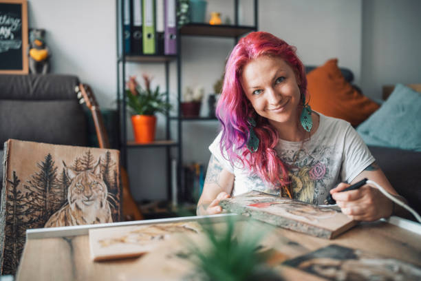 istock Portrait Of Smiling Graphic Artist Looking At The Camera While Drawing With Pyrograph On A Wooden Plank 1327795555