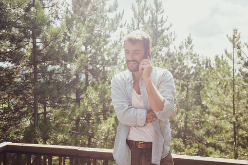 An image of a casually dressed young man making a phone call from his vacation cottage.