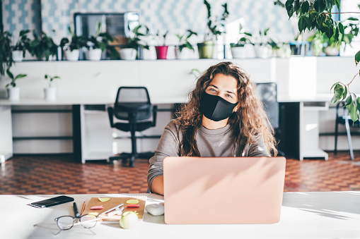 Mujer freelancer que usa máscara protectora y usa computadora portátil en una oficina cómoda, co-working verde en el lugar de trabajo moderno. photo