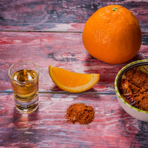 мексиканский напиток mezcal с дольками апельсина, перцем чили и солью червей в оахаке, мексика. старый потрепанный разноцветный стол - tequila shot стоковые фото и изображения