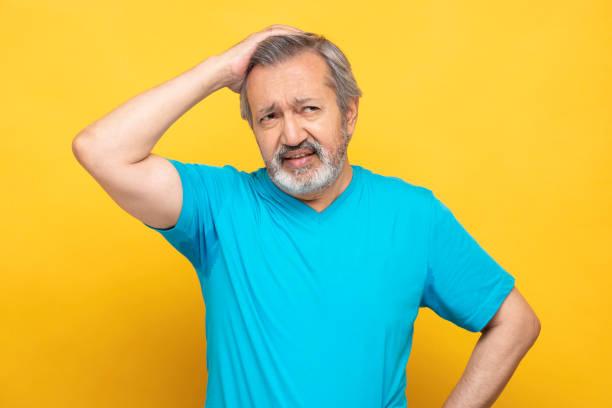 retrato de homens maduros em pé isolados sobre fundo amarelo:- foto de estoque - confusion hand in hair tired touching - fotografias e filmes do acervo