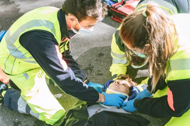 3 paramedics using a collar to immobilize a woman laying down on a road