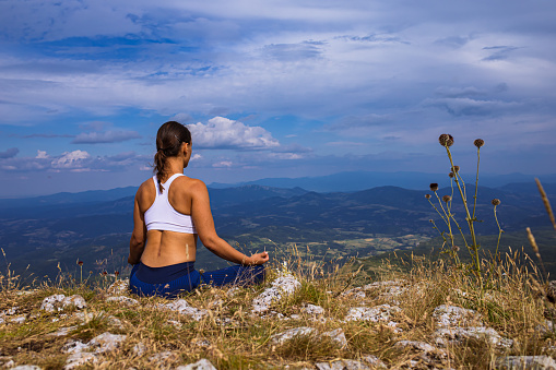 At the top of the mountain, a serene young woman meditating in a lotus position