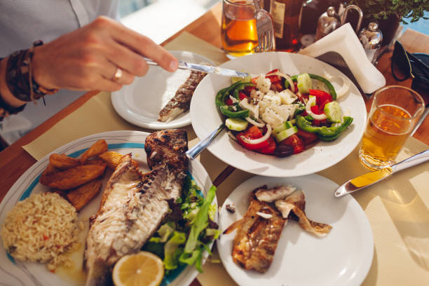 istock Man eats fish with vegetables and greek salad in outdoors restaurant. Fresh seafood dinner. 1327808871