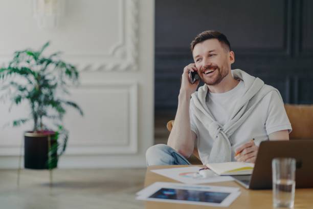 istock Happy freelancer talking on phone sitting at his work desk at home office 1327809115