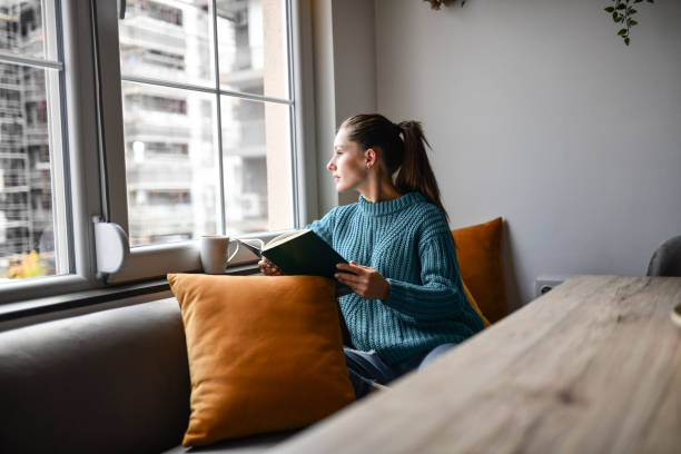 istock Cute Female Contemplating Book Story While Drinking Coffee By Window 1327809193
