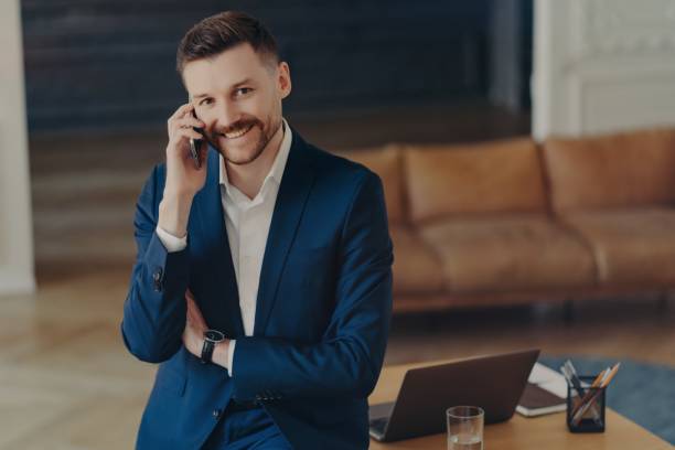 istock Smiling male entrepreneur talking on mobile phone while leaning on office desk 1327809956