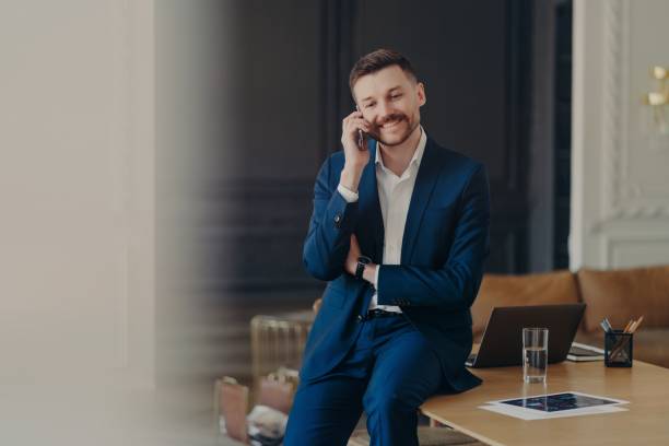 istock Happy handsome businessman talking on phone while sitting on office desk 1327809988