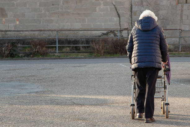 Grandma with wheeled walker. architecture background crumbling due to neglect in a depressed area district industry ruins. Old-age poverty concept anciana, mujer mayor con rollator para dar un paseo por la calle. abuela con andador de ruedas. fondo de la arquitectura que se desmorona debido a la negligencia en un área deprimida ruinas de la industria del distrito. concepto de pobreza de la vejez