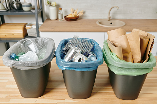 Row of three trash bins with sorted garbage on kitchen table