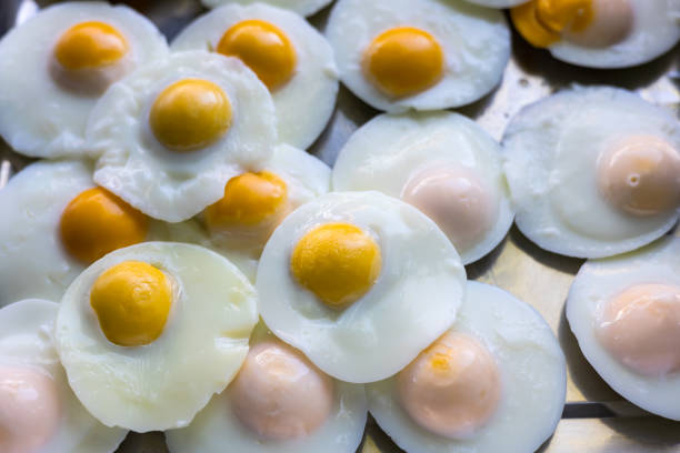 Close-up view of many poached and fried eggs without oil, with an appetizing shine lined up on aluminum trays in a restaurant in rural Thailand.