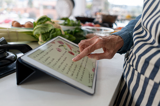 Close-up on a woman following a recipe online on a digital tablet while cooking at home - domestic life concepts. **DESIGN ON SCREEN WAS MADE FROM SCRATCH BY US**