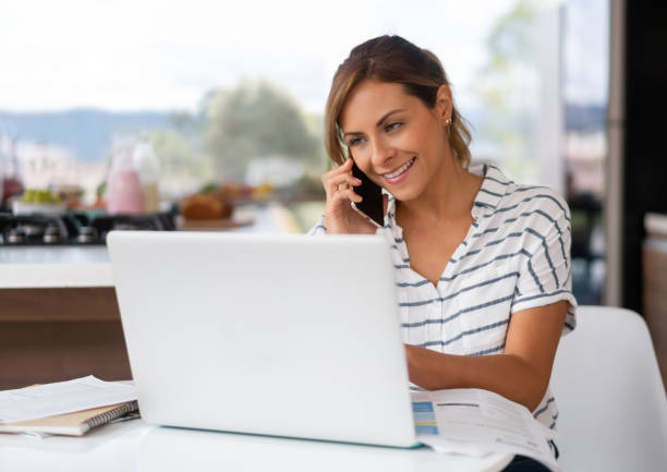 istock Woman talking on the phone while working at home on her laptop computer 1327820333