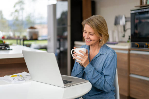 istock Happy woman at home drinking coffee while talking on a video call 1327820387