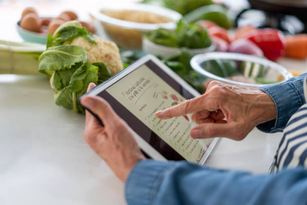 frau, die ein kochrezept online auf einem tablet-computer liest - cookbook recipe book old stock-fotos und bilder