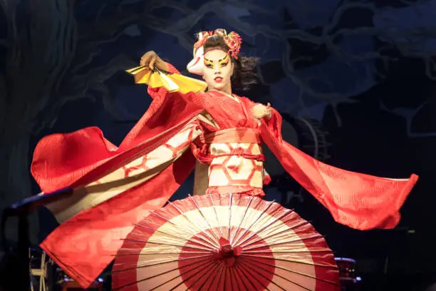 Photo of Woman dances with a fan and umbrella, with flowing sleeves. Traditional Japanese performance red fox dance. Kino Kitsune fox is a character in Japanese legends.