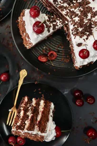 Stock photo showing an elevated view of plates containing sliced, homemade, luxury, Black Forest gateau. Served on black plates on a black surface surrounded by gold cutlery.