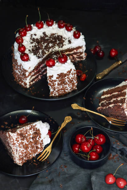 istock Image of sliced Black Forest gateau with piped whipped cream rosettes with morello cherries, luxury chocolate cake frosted with whipped cream and covered with chocolate shavings, black plate, black background, elevated view, focus on foreground 1327824257