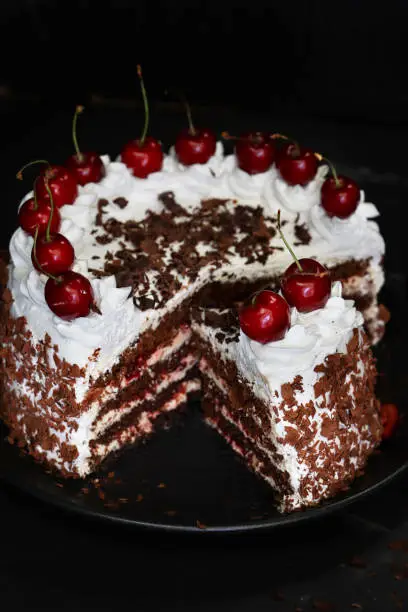 Stock photo showing a sliced, homemade, luxury, Black Forest gateau displayed on a black plate against a black background.