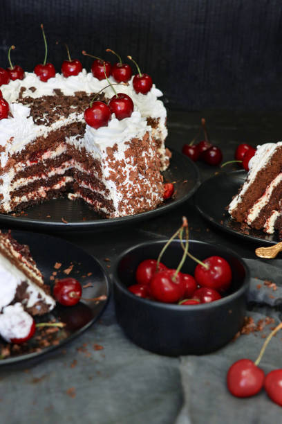 istock Image of sliced Black Forest gateau with piped whipped cream rosettes with morello cherries, luxury chocolate cake frosted with whipped cream and covered with chocolate shavings, black plate, black background, focus on foreground 1327824441