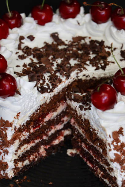 istock Full frame image of sliced Black Forest gateau with piped whipped cream rosettes with morello cherries, luxury chocolate cake frosted with whipped cream and covered with chocolate shavings, black plate, black background, focus on foreground, elevated view 1327824502
