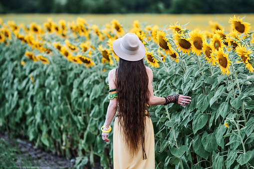 Beautiful woman with straw hat walking in sunflower field.